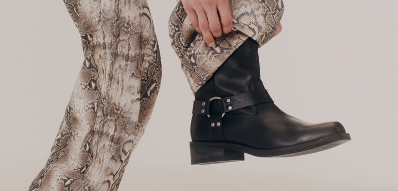 Μαύρη δερμάτινη μπότα έως τον αστράγαλο με στρογγυλή μύτη, χοντρό μεσαίο τακούνι και διακοσμητική ταινία με πόρπη. Συνδυασμένη με παντελόνι με σχέδιο από δέρμα φιδιού.