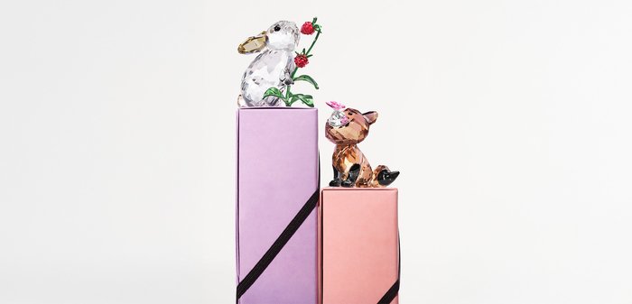 Zwei dekorative Kristalltierfiguren auf pinken und lilanen Boxen. Der Hase hält Grünzeug mit roten Blumen; der Fuchs hat eine pinkfarbene Akzentuierung.