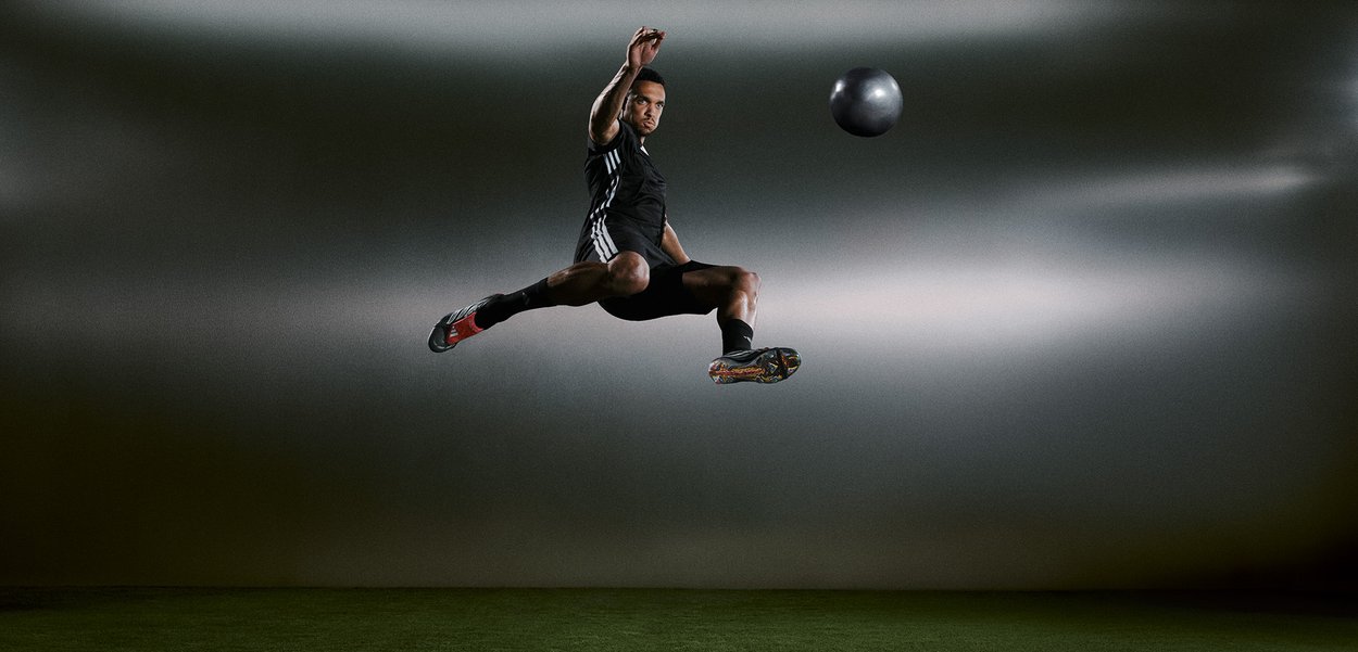 Idrottare i svart träningskläder hoppar i luften, boll i rörelse. Sportskor med färgglada accenter som framhäver den dynamiska rörelsen.