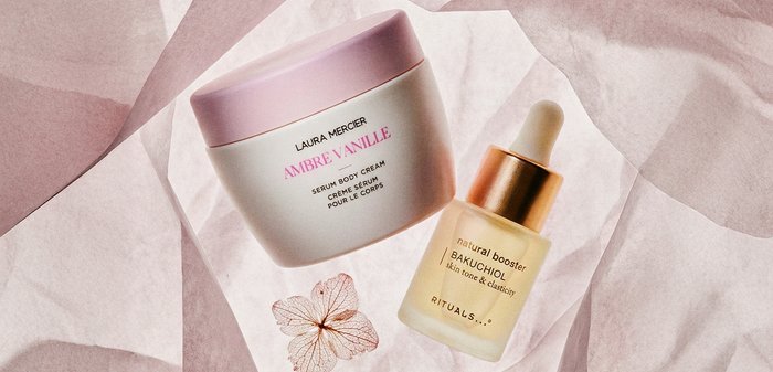 Pot de crème pour le corps Laura Mercier Ambre Vanille et flacon de sérum naturel booster Bakuchiol de Rituals avec pipette sur fond rose texturé.