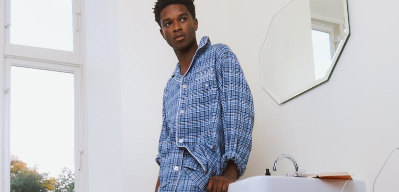 Ensemble de pyjama à carreaux bleu clair avec boutons blancs et poche poitrine. Coupe ample, tissu doux, exposé dans une pièce claire et minimaliste.