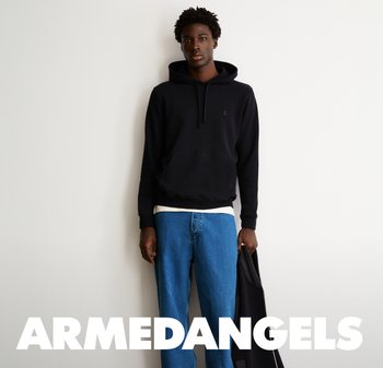 Schwarzer Kapuzenpullover mit einer Vorder Tasche, getragen über einem weißen Hemd, kombiniert mit blauen Jeans. Steht vor einem schlichten Hintergrund.