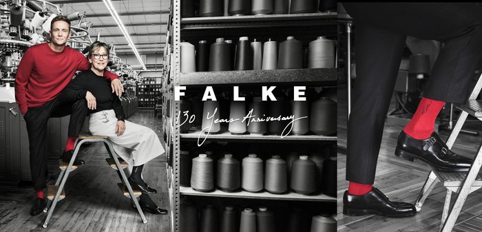 Mann und Frau in einer schwarz-weißen Fabrikumgebung, beide tragen rote Socken mit dem "Falke"-Logo und feiern das 130-jährige Jubiläum von Falke.