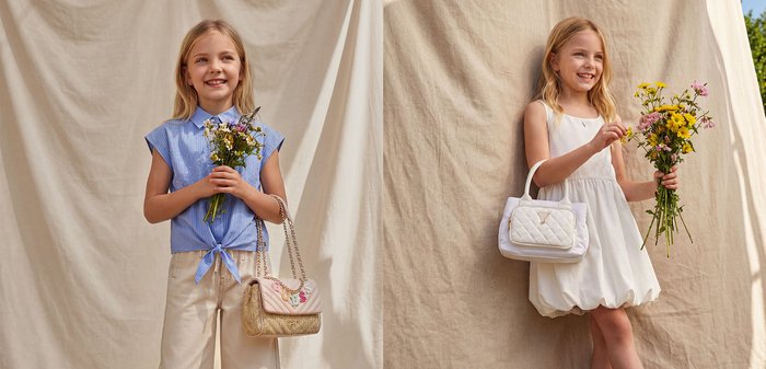 Jeune fille en robe blanche tenant un bouquet de fleurs jaunes et roses ainsi qu’un sac à main blanc, souriant devant un fond beige.