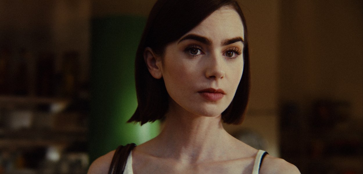 Joven con cabello corto y oscuro mira pensativamente hacia un lado en un ambiente interior con luz suave, vistiendo un top blanco con tirantes finos.