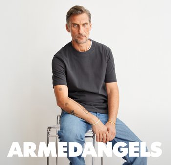 Kohleschwarzes Kurzarmhemd mit lockerer Passform, kombiniert mit hellblauen Jeans. Model sitzt auf einem transparenten Hocker vor einem schlichten Hintergrund.