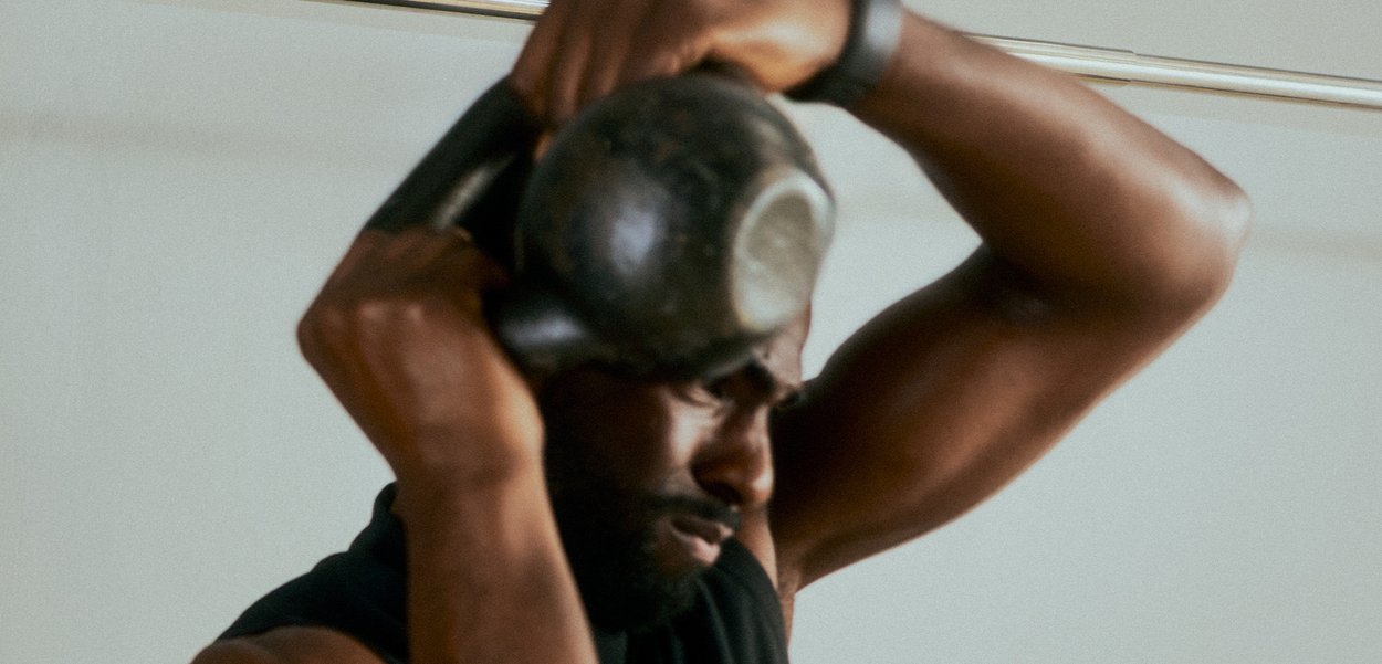 Homme levant un kettlebell noir au-dessus de sa tête, montrant un effort concentré lors d’un entraînement de force en intérieur.