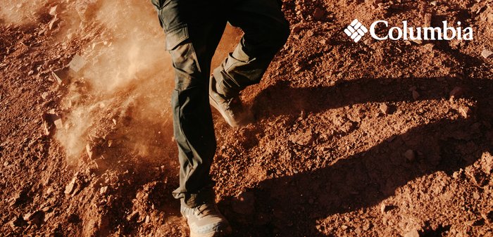 Columbia Outdoorhosen, dunkler Stoff, mit lockerer Passform und mehreren Taschen, getragen beim Gehen auf einem staubigen, felsigen Gelände.