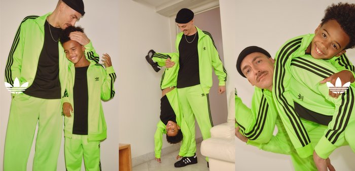 Fatos de treino adidas em verde neon com detalhes em preto, apresentando casacos com fecho éclair e calças ajustadas. Duas pessoas interagem de forma brincalhona.