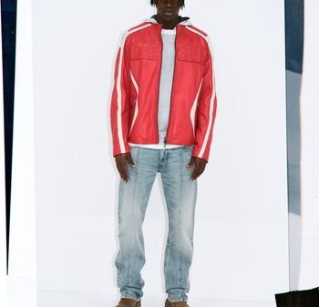 Uomo che indossa una giacca di pelle Diesel rossa e bianca, felpa grigia chiara, jeans blu sbiaditi e scarpe marroni, in piedi contro uno sfondo bianco.
