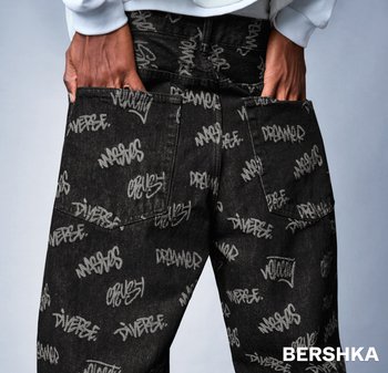 Černé džíny z denimu s potiskem ve stylu graffiti v bílé a světle šedé barvě. Mají výrazné zadní kapsy a střih s rovnými nohavicemi.