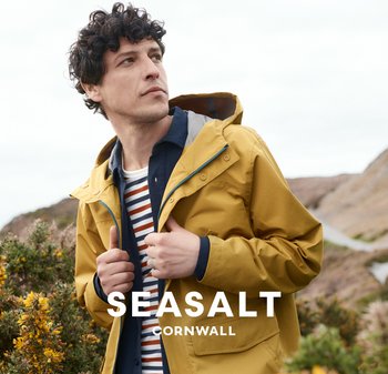 Žlutá voděodolná bunda s kapucí, s modrými akcenty. Pruhovaná košile pod ní. Přírodní krajina v pozadí.