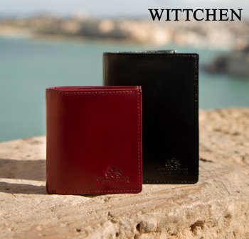 Zwei Lederbrieftaschen, eine rote und eine schwarze, stehen aufrecht auf einer Steinoberfläche vor einem verschwommenen Wasserhintergrund.