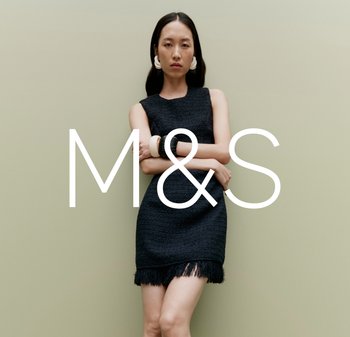 Robe noire texturée avec un ourlet frangé, portée par un mannequin. L'arrière-plan est d'un vert atténué. Grand logo "M&S" affiché de manière proéminente.