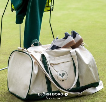 Sportväska i canvas med gröna detaljer, vita sneakers på toppen och gröna kläder hängande över ett närliggande stativ på en gräsmatta.