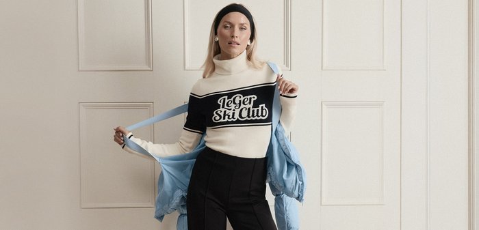 Maglione a collo alto color crema con strisce nere e testo "Le Ger Ski Club", abbinato a pantaloni sartoriali neri e una giacca a vento imbottita azzurro chiaro.