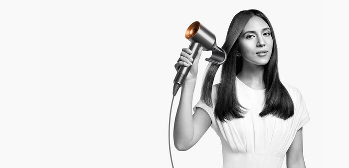 Föhn met een elegante zilveren behuizing en koperen accenten, voorzien van een tekstuur grip en een lange stroomkabel, vastgehouden door een persoon met steil haar.