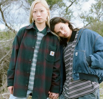Camisa de franela a cuadros en verde y burdeos, con un bolsillo en el pecho. Chaqueta de mezclilla con cierre frontal y puños acanalados. Camisetas de rayas debajo.