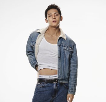 Jeansjack met sherpa kraag, blauwe kleur, gedragen over een wit tanktop. Donkerblauwe jeans, zichtbare Calvin Klein tailleband, relaxte pasvorm.