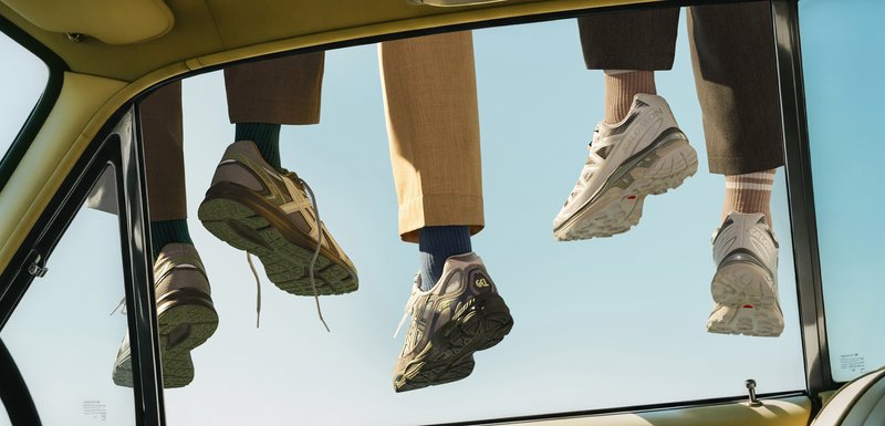 Quatre baskets présentées par le dessous, affichant des designs variés : accents beige et gris, semelles texturées et logos distincts ; accompagnées de chaussettes colorées.