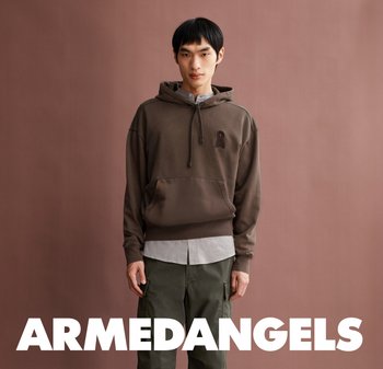 Junger Mann in braunem Hoodie und grünen Cargo-Hosen steht vor einem gedämpften braunen Hintergrund mit dem Text "ARMEDANGELS" darunter.