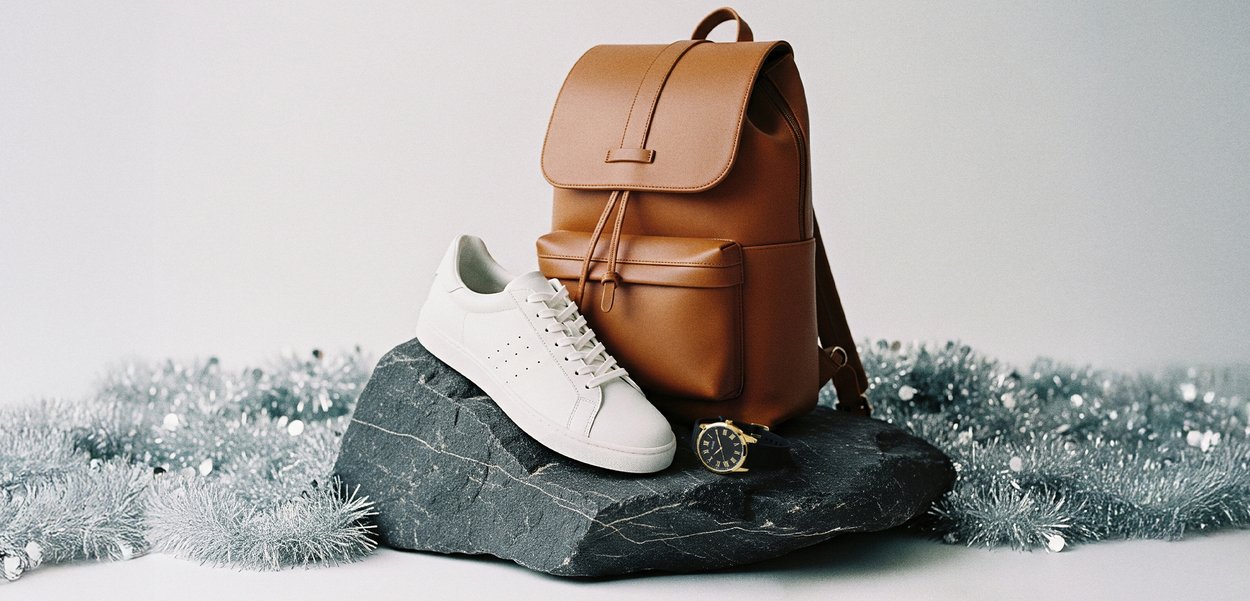 Καφέ δερμάτινος σακίδιο, λευκά αθλητικά παπούτσια και μαύρο ρολόι σε σκοτεινή πέτρινη επιφάνεια με ασημένιο γκλίτερ στο φόντο. Κλασικά στοιχεία σχεδίασης.