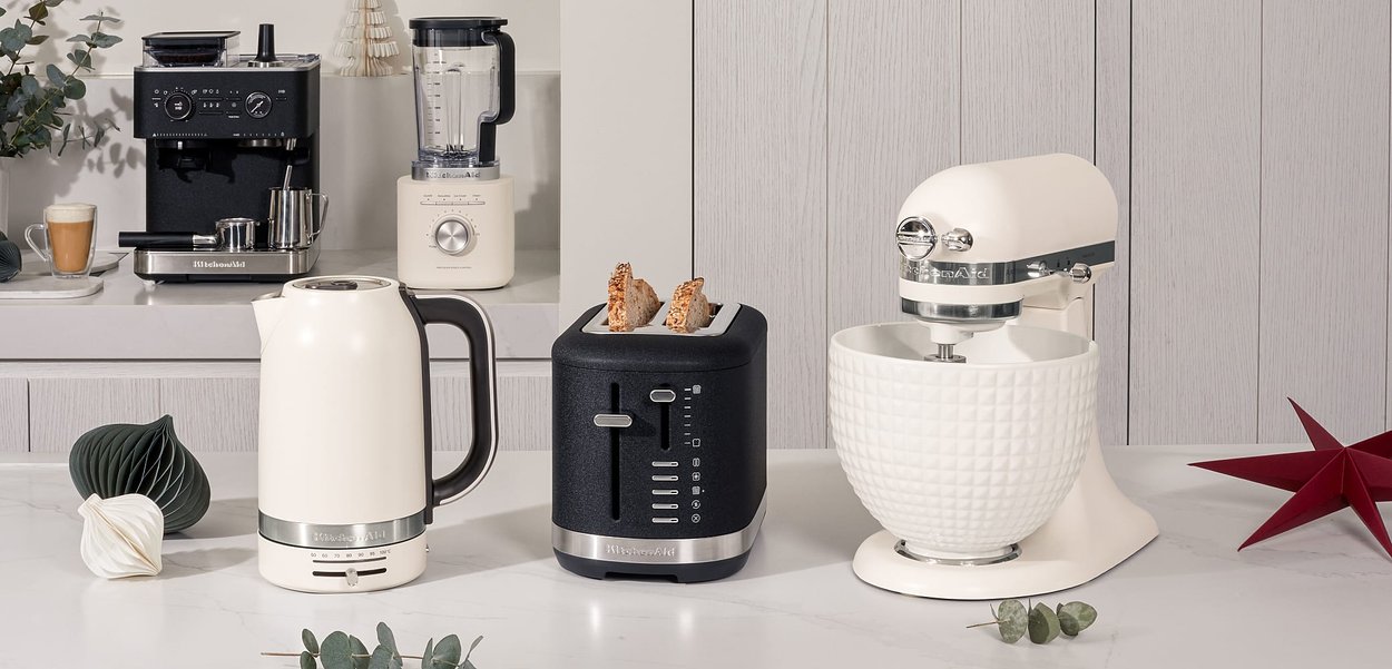 Bouilloire blanche, grille-pain noir à deux fentes avec minuterie, robot mixeur argenté avec un bol texturé, et un blender. Le tout dans une cuisine moderne.