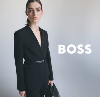 Blazer noir avec un décolleté en V profond et des manches longues, cintré à la taille par une ceinture, associé à un pantalon noir ajusté et un sac à main.