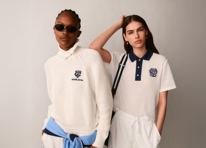 Deux femmes portant des vêtements de sport blancs de la marque Wimbledon, dont l'une avec des lunettes de soleil et une veste bleu clair nouée autour de la taille.