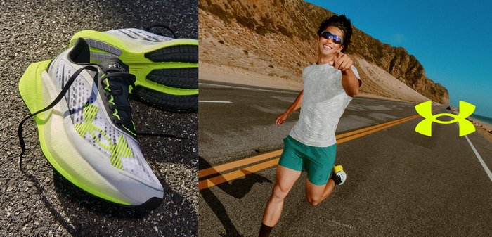 Zapatillas de correr con detalles en verde neón sobre el pavimento junto a un corredor sonriente con gafas de sol, camiseta gris y pantalones cortos verdes en una carretera de montaña.