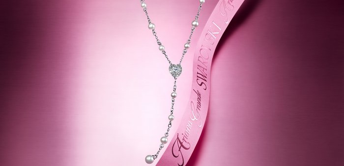 Swarovski-Halskette mit silberner Kette, herzförmigem Kristallanhänger und weißen Perlen. Ausgestattet mit einem pinken Band mit der Aufschrift "Ariana Grande".