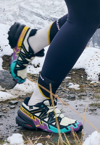 Παπούτσια τρεξίματος Salomon σε κρεμ, μαύρο και μωβ, με υφή στη σόλα, πολύχρωμες λεπτομέρειες και ασφαλές σύστημα κορδονιών.