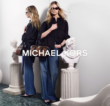 Zwarte oversized blouse, lichtblauwe jeans met wijde pijpen en een handtas met luipaardprint. Bril op, met een klassieke buste op een standaard ernaast.