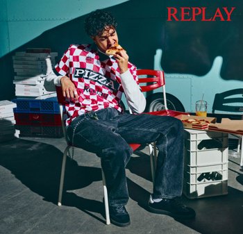 Camisa de cuadros roja y blanca con el texto "PIZZA", jeans negros, comiendo pizza, sentado en una silla roja. El fondo incluye cajas de pizza y una bebida.