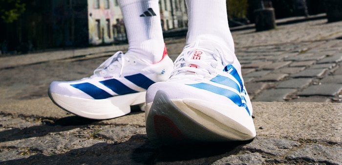 Personne portant des chaussures de sport blanches et bleues et des chaussettes blanches marchant dans une rue pavée en plein jour.