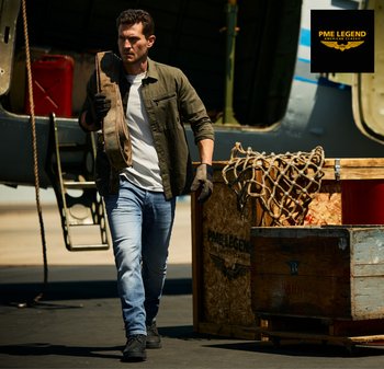 Man met handschoenen en casual kleding draagt een zware riem bij kratten en een open vrachtvliegtuig op een zonnige dag.