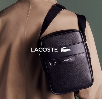 Bolso bandolera de cuero negro con acabado texturizado, que cuenta con un bolsillo delantero, herrajes plateados y un prominente logo blanco de Lacoste.