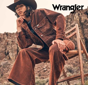 Wrangler brun kordfløyelsjakke med matchende vide bukser. Teksturert stoff, knappelukking og synlige sømmer. Bakgrunn med en trestol.