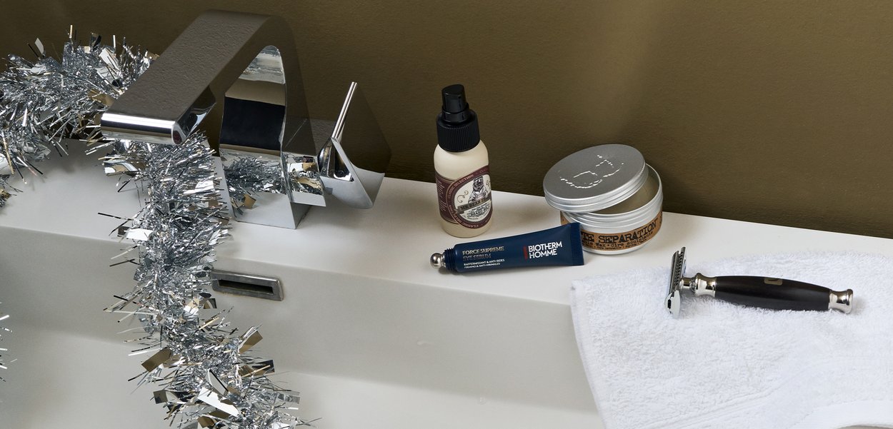 Chrom-Wasserhahn mit elegantem Design, silbernem Lametta, weißem Handtuch, Rasierer mit dunkelholzfarbenem Griff, Hautpflegeprodukte in verschiedenen Behältern.