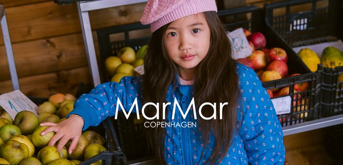 Jovem menina com um chapéu cor-de-rosa e uma jaqueta azul a escolher fruta em caixas num mercado de madeira.