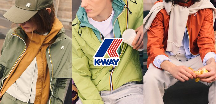 Vier Personen sitzen draußen auf einer Bank und tragen bunte Jacken, eine Person streichelt einen Hund in einem grünen Mantel.