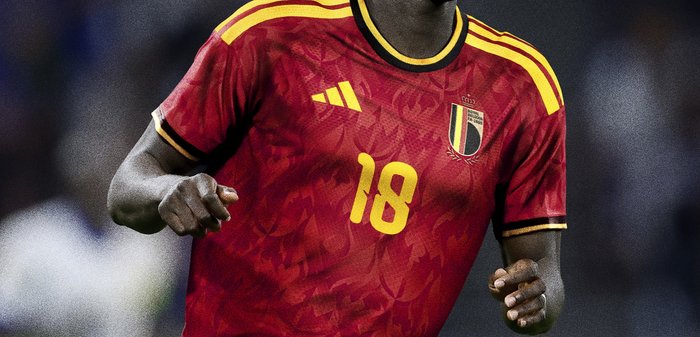 Joueur de football portant le maillot rouge et jaune de l'équipe nationale belge avec le numéro 18 courant sur le terrain pendant un match.