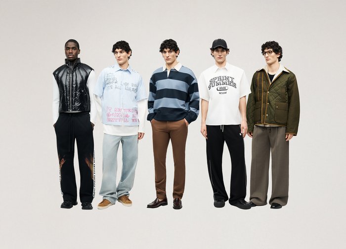 Πέντε άντρες στέκονται δίπλα ο ένας στον άλλο φορώντας καθημερινά, διαφορετικά ρούχα, συμπεριλαμβανομένου ενός μαύρου γιλέκου, ενός ανοιχτόχρωμου μπλε πουκάμισου, μιας ριγέ ζακέτας, μιας λευκής μπλούζας με τύπωμα και ενός καπιτονέ μπουφάν.