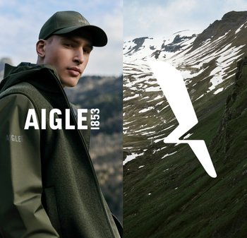 Gilet et casquette verts de Aigle 1853, avec fermeture éclair et tissu texturé. L'arrière-plan montre des montagnes enneigées et des pentes verdoyantes.