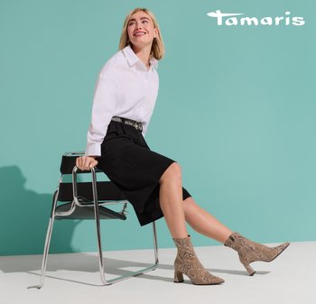 Beige ankle boots with a textured snake skin pattern, pointed toe, and block heel. Model wears a white shirt and black skirt, seated.