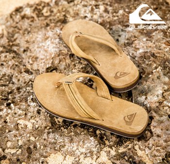 Tongs marron en finition suédée, dotées d'un logo distinctif sur la semelle intérieure et de deux fines brides. Semelle texturée, adaptées pour un usage décontracté.