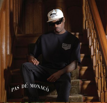 Svart oversized t-skjorte med logo på framsiden, mørke jeans, hvit baseballcaps og solbriller, sittende på tretrapper med dekorativt teppe.