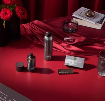 Mørkerød bord med røde roser, herreskincare-produkter, et glas med kirsebærdrik, stak bøger og en træ Rituals-accessory.