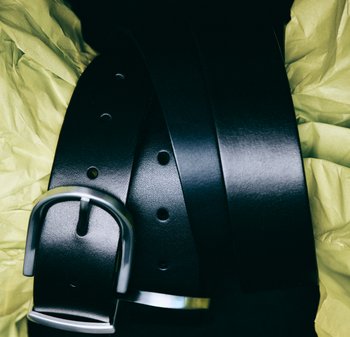 Tre sorte læderbælter med en glat overflade, med metalspænder og jævnt fordelt huller, lagt på krøllet gult silkepapir.