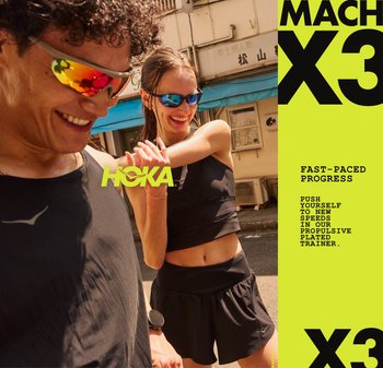Schwarze Sportoberteile und Shorts an zwei Personen, die reflektierende Sonnenbrillen tragen. Im Hintergrund ist ein Gebäude mit blauer Markise zu sehen. HOKA-Branding ist sichtbar.